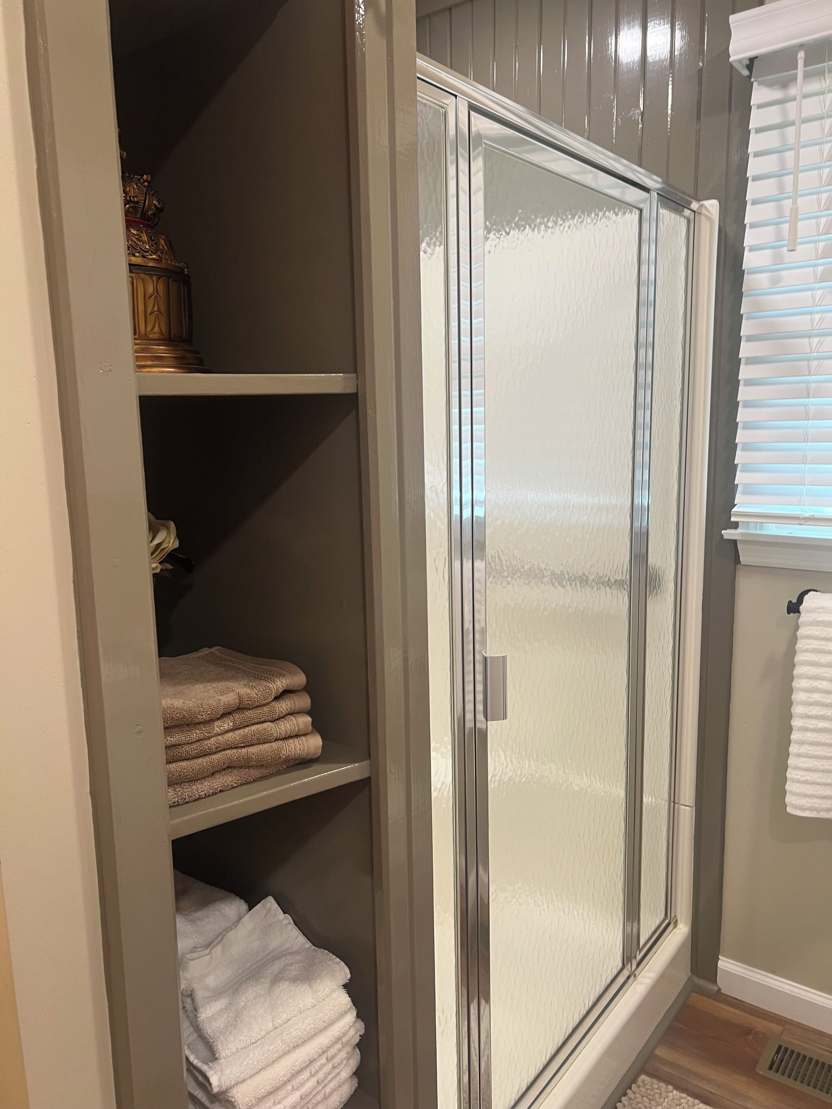 A walk-in closet with a mirrored closet door, shelves with folded towels, and a window with blinds.