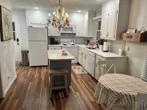 A kitchen with white cabinets, a wooden floor, a chandelier, and a dining area with a table. - Charming cottage, minutes from Cummins Falls and downtown Cookeville, TN.   (Cookeville)
