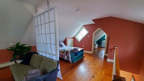 Una habitación con piso de madera, una cama con colcha colorida, una silla azul y una ventana.