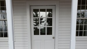 Una puerta blanca con un panel de vidrio, un felpudo y un porche de madera.
