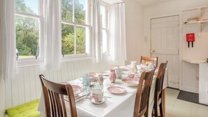 Un coin repas avec une table dressée pour quatre personnes, des murs blancs et une vue sur la verdure à l’extérieur.