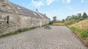 Un bâtiment en pierre avec une allée gravillonnée et une table de pique-nique.