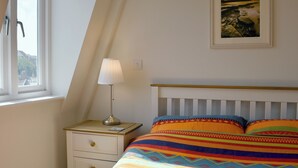 A bedroom with a bed, a nightstand, a lamp, a window, and a framed picture on the wall. - 1 bedroom accommodation in Swanage (Swanage)