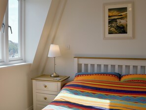 A bedroom with a bed, a nightstand, a lamp, a window, and a framed picture on the wall. - 1 bedroom accommodation in Swanage (Swanage)