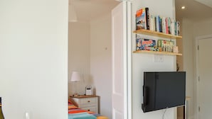 A bedroom with a bed, bedside table, lamp, and a TV mounted on the wall. - 1 bedroom accommodation in Swanage (Swanage)