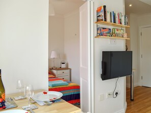Quarto com cama, mesa de cabeceira, luminária e televisão na parede.