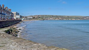 A coastal town with a stone promenade, buildings along the shore, and a view of the sea and hills in the distance. - 1 bedroom accommodation in Swanage (Swanage)