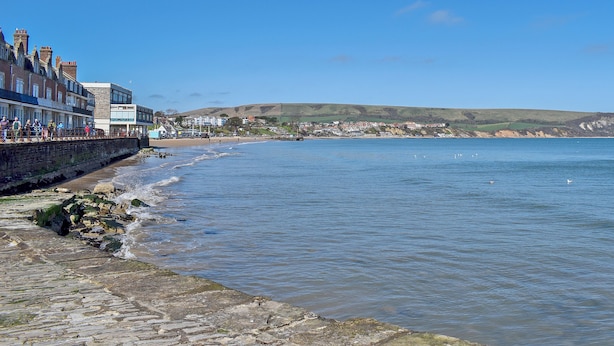 A coastal town with a stone promenade, buildings along the shore, and a view of the sea and hills in the distance. - 1 bedroom accommodation in Swanage (Swanage)
