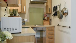 A compact kitchen with wooden cabinets, a stainless steel range hood, a built-in oven, and a small countertop. - 1 bedroom accommodation in Swanage (Swanage)