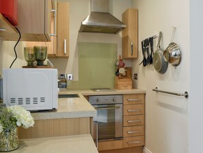 A compact kitchen with wooden cabinets, a stainless steel range hood, a built-in oven, and a small countertop. - 1 bedroom accommodation in Swanage (Swanage)