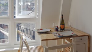 A dining area with a table set for two, a bottle of Prosecco, and a view of the city through large windows. - 1 bedroom accommodation in Swanage (Swanage)