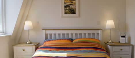 Un dormitorio con una cama, dos mesitas de noche, una lámpara, una radio y un cuadro en la pared.