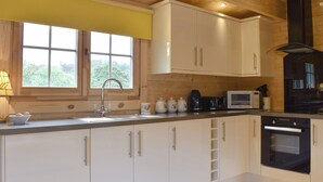 A modern kitchen with white cabinets, a stainless steel sink, a microwave, and a black oven. - Brook Cottage - UK12643 (Sleights near Whitby)