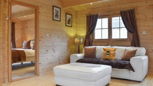 A cozy cabin interior with a white sofa, a small ottoman, wooden walls, a mirror, and a window with curtains. - Brook Cottage - UK12643 (Sleights near Whitby)