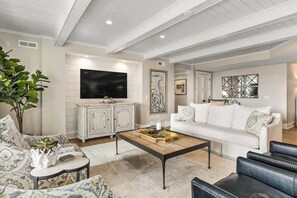 Un salon avec un canapé blanc, une table basse, un téléviseur et un meuble.