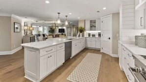 A spacious kitchen with white cabinetry, a large island, pendant lighting, and a wooden floor. - Luxury Oceanfront Villa w/ Pool & Spa Hilton Head (Hilton Head Island)