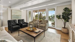 A spacious living room with a large window, a coffee table, two sofas, and a potted plant. - Luxury Oceanfront Villa w/ Pool & Spa Hilton Head (Hilton Head Island)