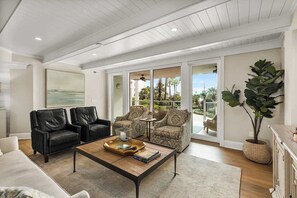 A spacious living room with a large window, a coffee table, two sofas, and a potted plant.