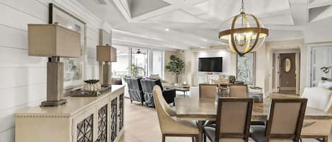 A spacious living room with a large dining table, comfortable seating, and a modern chandelier.