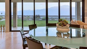 A modern dining area with a glass table and chairs, a decorative centerpiece, and a large window offering a view of a grassy landscape and mountains.
