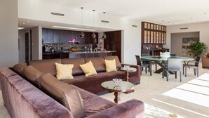 A modern living room with a brown sofa, a glass coffee table, and a dining area with a glass table and chairs.