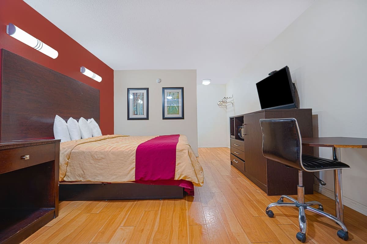 A hotel room with a bed, a desk, a chair, a TV, and a dresser.
