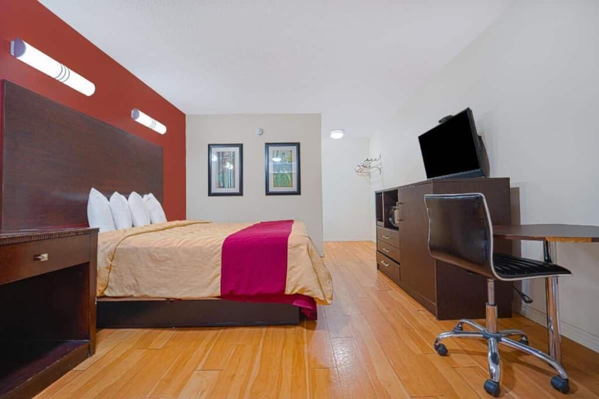 A hotel room with a bed, a desk, a chair, a television, and two framed pictures on the wall.