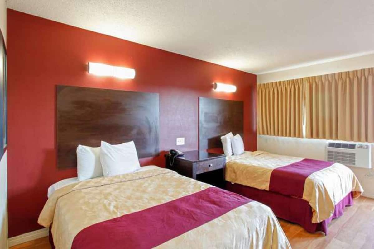 A hotel room with two beds, a large mirror, and a window with curtains.