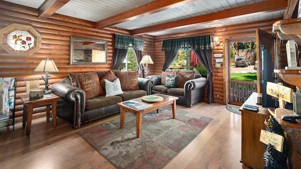 Interior acolhedor de uma cabana de madeira com teto de madeira, dois sofás de couro, uma mesa de centro e decoração rústica.