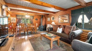 Interior de uma cabana de tronco com uma mesa de jantar de madeira, cadeiras, um sofá e uma lareira.