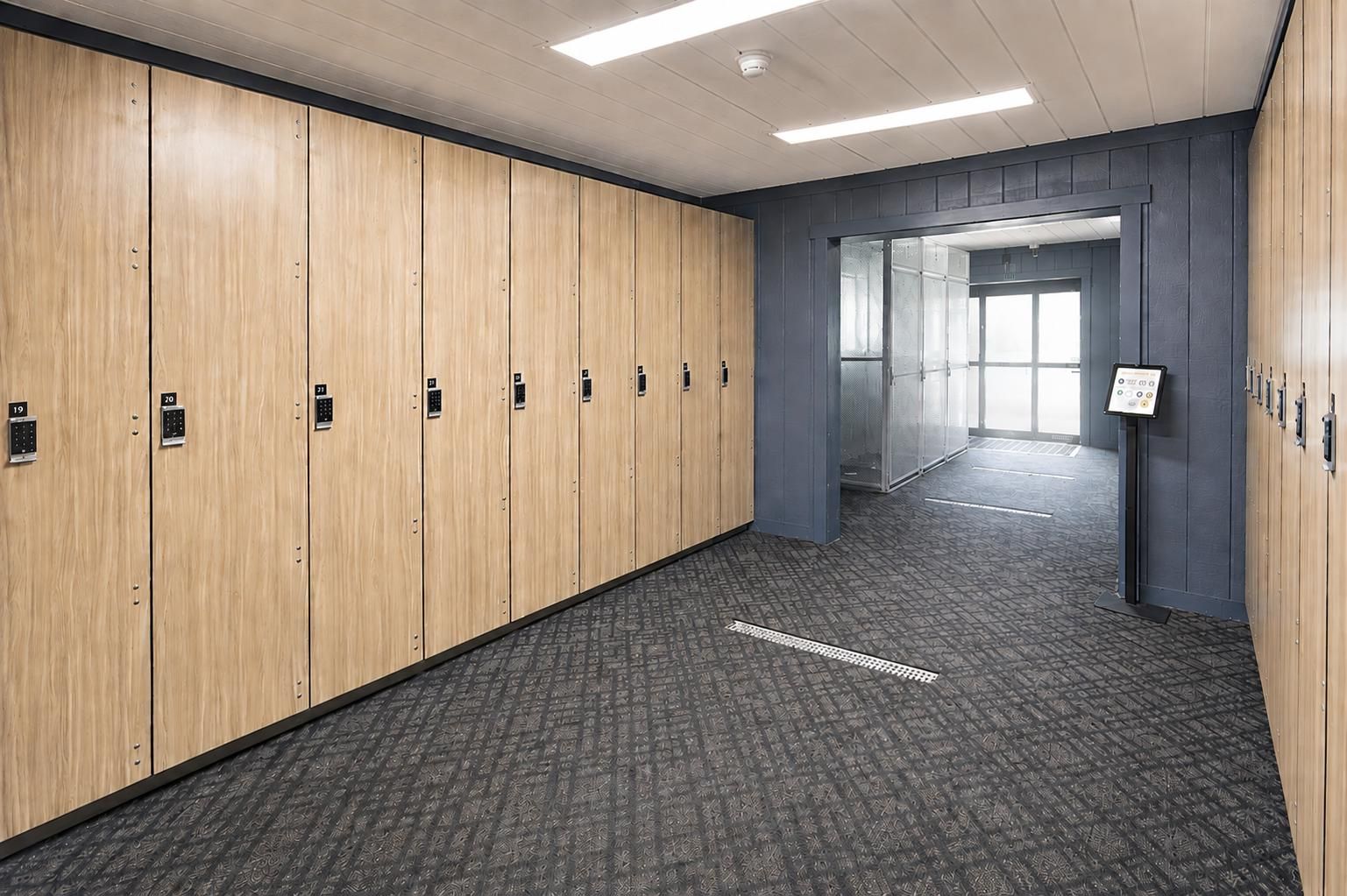 Een rij houten lockers met genummerde sleutels, een grijs geweven vloerkleed en een gang die leidt naar een lichte kamer met grote ramen.