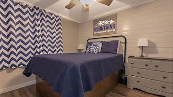 Une chambre à coucher comprenant un lit, une commode, une table de chevet, une lampe et un tableau décoratif mural.