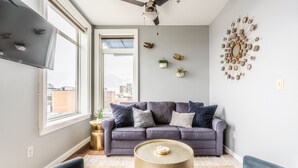 A modern living room with a grey sofa, two armchairs, a round coffee table, and decorative wall art. - Cozy Belltown Condo with amazing Elliott Bay Views (Seattle)
