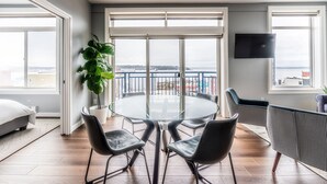 A modern living room with a glass table, two black chairs, a potted plant, a sofa, and a TV on the wall. - Cozy Belltown Condo with amazing Elliott Bay Views (Seattle)
