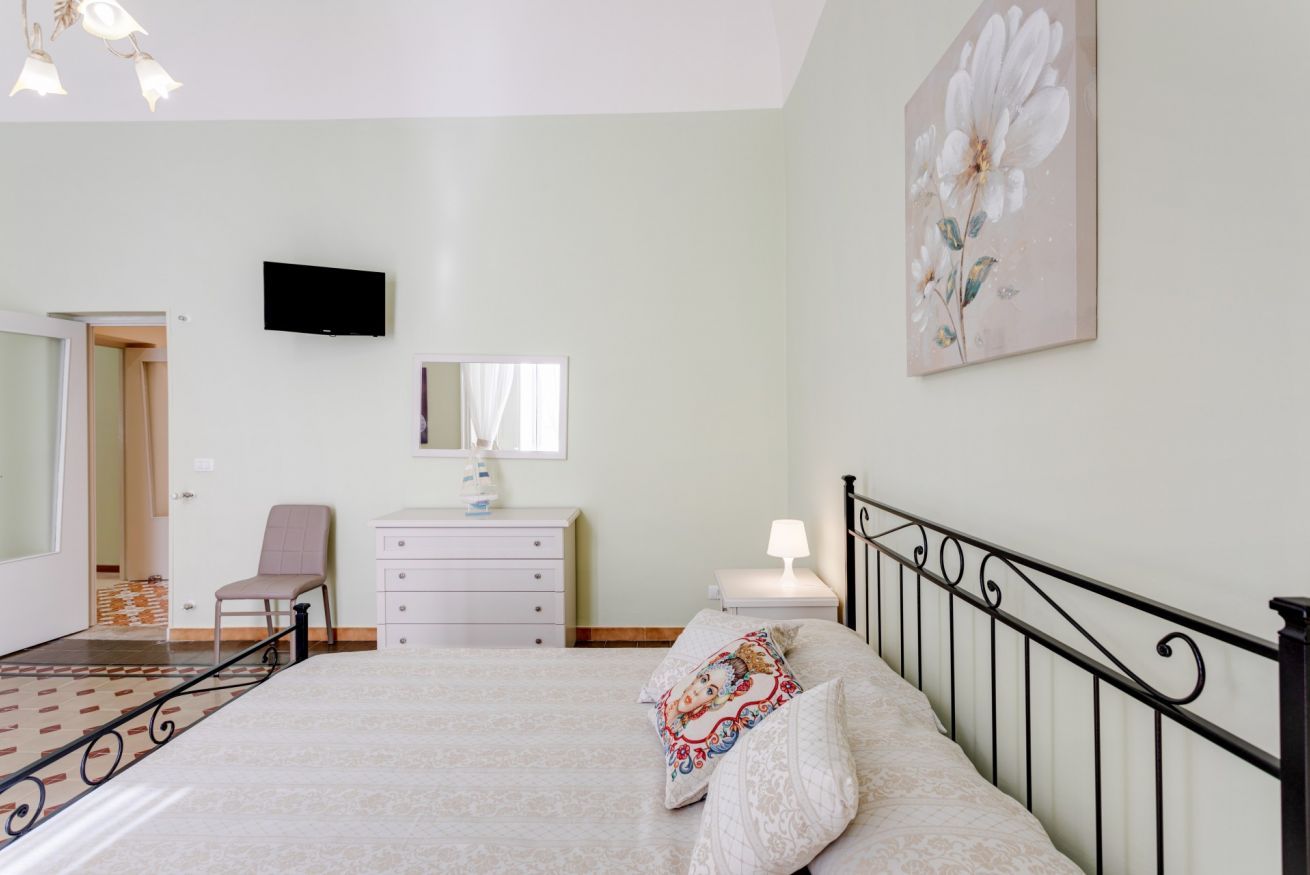 Une chambre à coucher comprenant un lit, une chaise, une commode, une table de chevet avec une lampe, un téléviseur fixé au mur et un tableau.