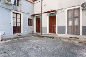 A courtyard with stone flooring, a small window, and a door with a brown door frame.