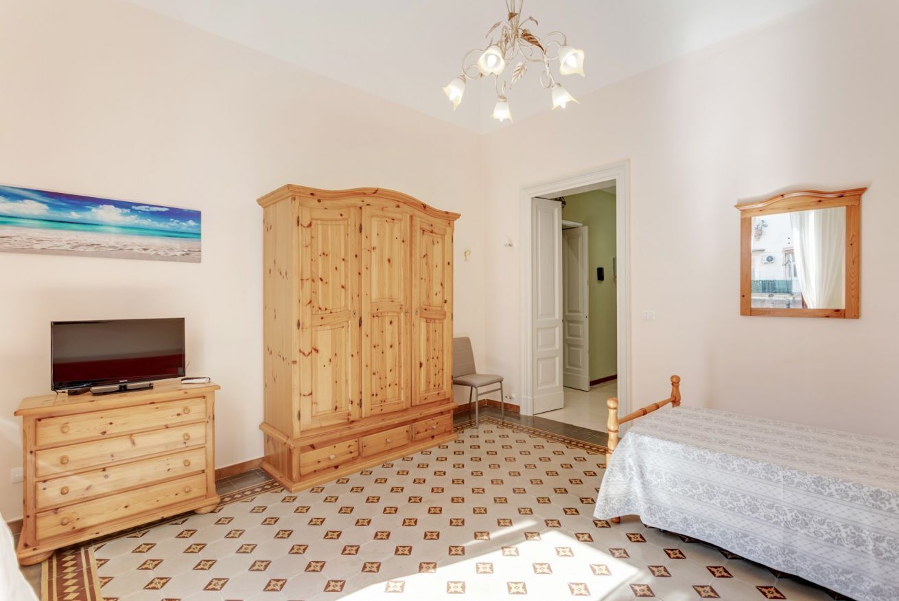 Een slaapkamer met een houten garderobe, een televisie op een dressoir, een bed met een witte dekbedovertrek en een vloer met een patroon.