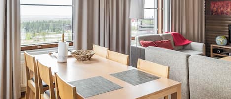 A modern living room with a dining table, chairs, a sofa, and a television.