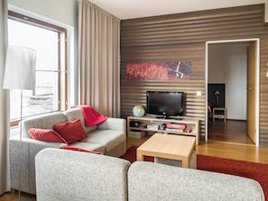 Un salon moderne avec un canapé gris, des coussins rouges, un téléviseur à écran plat et une table basse en bois.