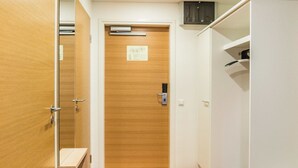 A hotel room with a wooden door, a striped carpet, a white wardrobe, and a small shelf.