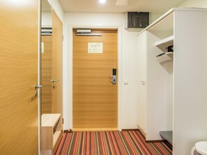 A hotel room with a wooden door, a striped carpet, a white wardrobe, and a small table.