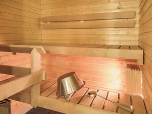 A sauna with wooden benches and a metal bucket.