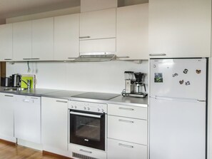A modern kitchen with white cabinets, a built-in oven, a coffee maker, and a refrigerator with magnets.