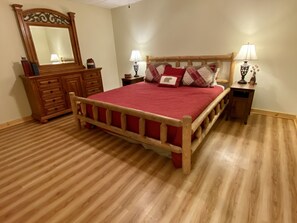 A bedroom with a wooden bed, a dresser, a mirror, two bedside tables with lamps, and a red bedspread. - Riverfront Mtn Retreat Hot Tub/Fireplaces/King Beds/Tubing/Fishing/Spacious (Ellijay)