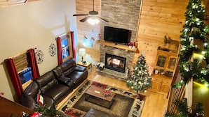 A cozy living room with a fireplace, leather sofa, and a Christmas tree. - Riverfront Mtn Retreat Hot Tub/Fireplaces/King Beds/Tubing/Fishing/Spacious (Ellijay)