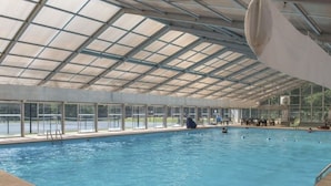 An indoor swimming pool with a glass ceiling, surrounded by a pool deck and a view of the outdoors. - Riverfront Mtn Retreat Hot Tub/Fireplaces/King Beds/Tubing/Fishing/Spacious (Ellijay)