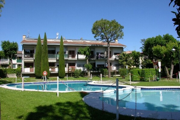 A hotel with a swimming pool, a large building with multiple balconies, and a well-maintained lawn.