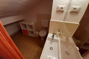 A small bathroom with a white sink, toilet, and a shelf unit.