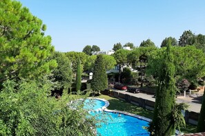 A swimming pool surrounded by lush greenery and tall trees, with a view of residential buildings in the background.