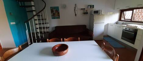 A dining area with a white table, brown chairs, a brown bowl, a spiral staircase, a kitchen with white cabinets, a microwave, and an oven.